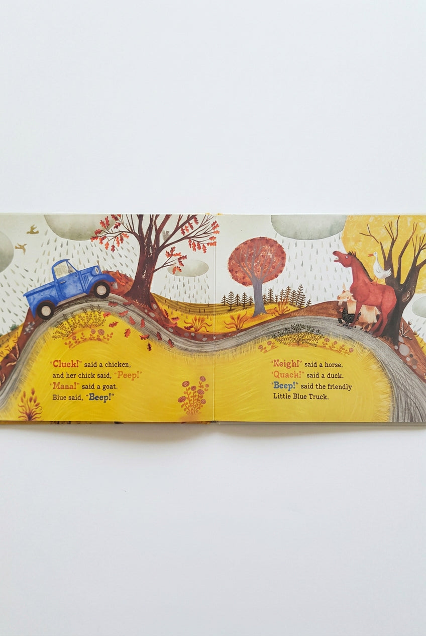 Illustrated book page with a blue truck, horse, duck, and cow on a road with autumn trees and leaves.