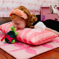 Child with red hair and a pink headband lying on a pink pillow with a turtle plush toy.